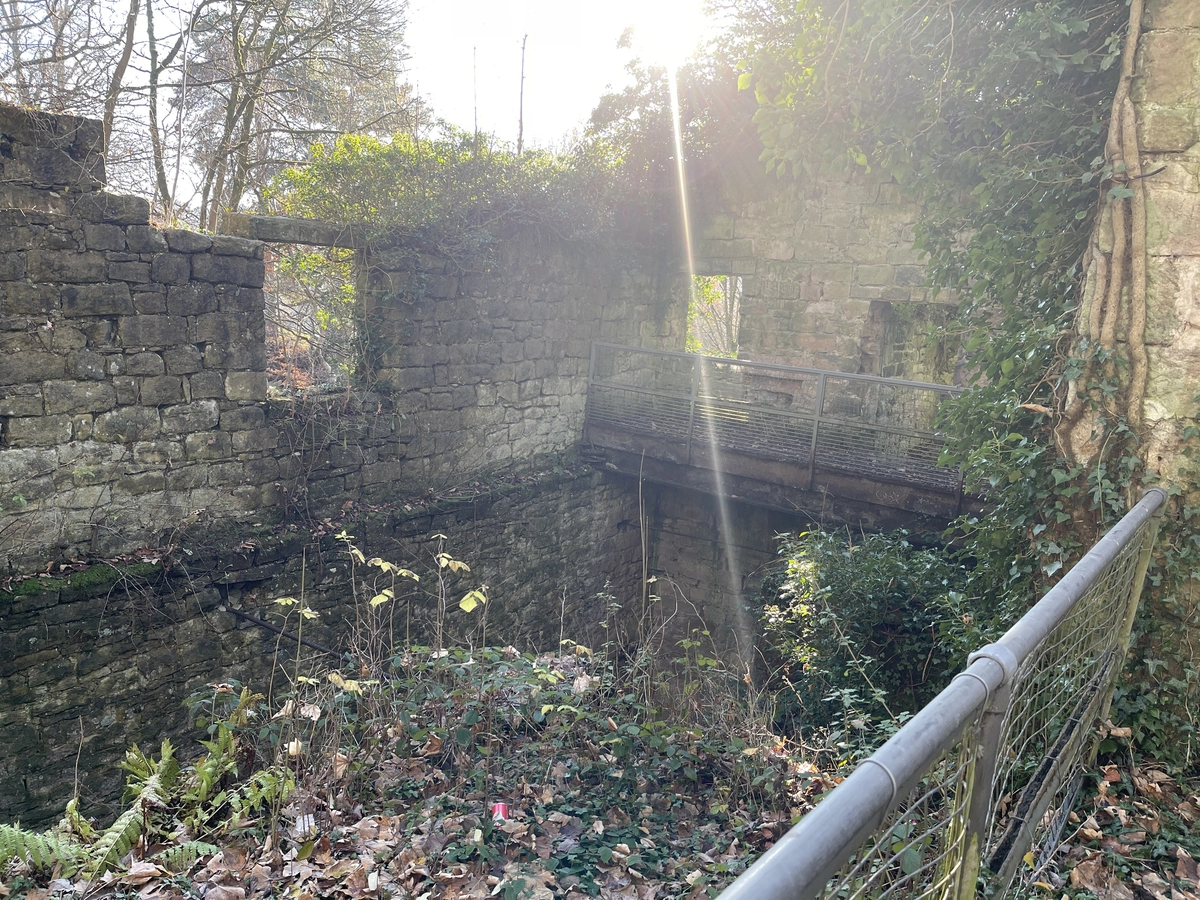 The ruins seen across a railing, with a footbridge over the pit